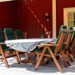 Holztisch mit sechs grünen Stühlen auf einer Terrasse vor einem roten Gebäude.