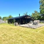 Moderne Hütte mit Terrasse, Garten und Grillplatz. Umgeben von Bäumen und Zaun.