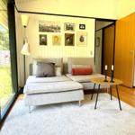 Ein Wohnzimmer mit Sofa, Tisch und Wanddekoration. Große Fenster und Holzboden.