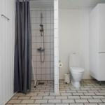Badezimmer mit Dusche, Toilette und Fenster. Weiße Wände und Fliesen.