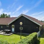 Ein dunkles Holzhaus mit Terrasse, Garten und rotem Dach unter blauem Himmel.