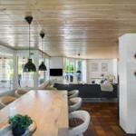 Essbereich mit langem Tisch, Sofa im Hintergrund und Poolbereich durch Fenster sichtbar.