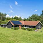 Haus mit Solaranlage, Garten und Schaukel. Umgeben von Bäumen unter blauem Himmel.