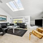 Wohnzimmer mit schwarzen Ledermöbeln, Holzboden und Dachfenstern. Gelber Sessel und Fernseher sichtbar.