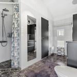 Badezimmer mit Dusche, Toilette und Waschbecken. Graue Fliesen und moderne Einrichtung.