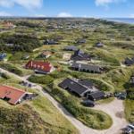 Aerielansicht von Häusern auf grünen Dünen mit Blick aufs Meer.