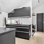Küche mit schwarzen Schränken, Arbeitsplatte und Spüle. Hintergrund: Flur mit Tür und Schuhregal.