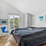 Schlafzimmer mit Bett, blauer Stuhl und Blick auf Grasflächen.