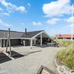 Haus mit Terrasse, Spielplatz und dänischer Flagge vor grüner Vegetation.