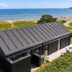 Modernes Haus mit Terrasse und Meerblick. Umgeben von Grünflächen und Strand.