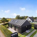 Moderne schwarze Villa mit großem Garten und Blick auf Wasser.