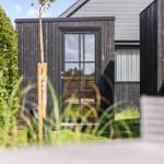 Schwarze Holzhütte mit Glasfront und Garten. Moderne Architektur im Freien.