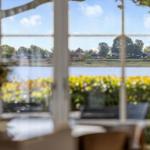 Durch ein Fenster blickt man auf einen See mit Uferhäusern und Bäumen.