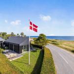 Moderne Villa mit Terrasse, Flagge und Meerblick. Grünhedge und asphaltierter Weg.