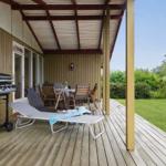 Terrasse mit Grill, Liegestuhl und Tisch mit Stühlen. Grünflächen im Hintergrund.