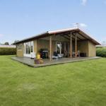 Moderne Ferienhaus mit Terrasse, Grill und Garten. Sicht auf grünen Rasen und Hecken.