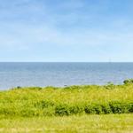 Grünes Feld mit Blick auf das Meer und zwei Segelboote im Hintergrund.