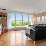 Wohnzimmer mit Holzwänden, großem Fenster und schwarzem Sofa.