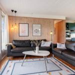 Wohnbereich mit zwei schwarzen Sofas, Holzwand und großem Fenster. Küche im Hintergrund.