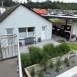 Haus mit Terrasse, Garten und geparktem Geländewagen. Blick auf Wohngebiet und Wald.