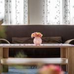 Ein Wohnzimmer mit braunem Sofa, Holztisch und Blumen in einem Vasen.