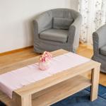Ein Wohnbereich mit zwei grauen Sesseln, einem Holztisch und einem Blumenarrangement.