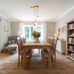 Esszimmer mit Holztisch, Stühlen und Bücherregal. Fenster mit Blick ins Freie.