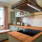 Küche mit Holzplatten, grünen Schränken und Fensterbank mit Stoffbezug.