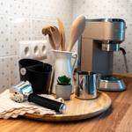 Küchenbereich mit Espressomaschine, Holzbrett und Küchenutensilien auf Holzoberfläche.