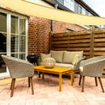 Terrasse mit Sitzgruppe, Grill und Sonnensegel. Holzgeländer und Ziegelwand.