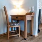 Schreibtisch mit Stuhl und Lampe an der Wand. Holzfußboden und Sessel im Hintergrund.