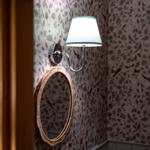Wand mit floraler Tapete, runder Spiegel und Wandlampe mit Schirm