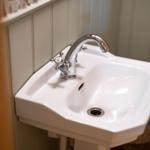 Weißes Waschbecken mit Chromarmatur an vertikal verkleideter Wand.