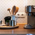 Küchenarbeitsfläche mit Kaffeemaschine, Holzlöffeln und Pflanze.