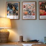 Wand mit drei gerahmten William Morris Poster, Lampe, Kerze und Uhr auf einem Tisch.