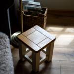 Holzstuhl mit quadratischer Sitzfläche auf Holzboden neben einem Sitzmöbel.