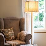 Ein Sessel mit Kissen und Fell liegt neben einem Stehlampe vor einem Fenster.