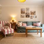 Wohnzimmer mit Sofa, Sessel, Tisch und Wandbildern.
