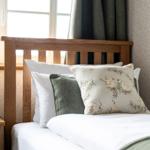 Ein Bett mit Holzkopfteil, Kissen und Nachttisch neben Fenster.