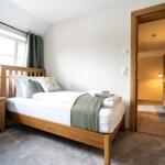 Ein Schlafzimmer mit Holzbett, Nachttisch und Fenster. Durchgang zu Badezimmer.