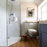 Bad mit Dusche, Toilette und Waschbecken. Holzboden und Wandbild mit Schaf.