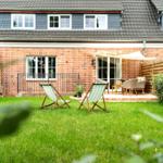 Hinterhof mit Grasfläche, zwei Liegestühlen und Terrasse mit Sitzgelegenheiten.
