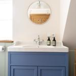 Badezimmer mit blauem Waschbecken, runden Spiegel und Holzregal.