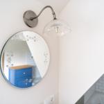 Runde Spiegelfläche mit floralen Mustern und Wandlampe mit Glasdiffusor.