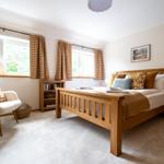 Schlafzimmer mit Holzbett, Fenstern mit karierten Vorhängen und einem Sessel.