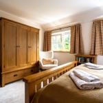 Schlafzimmer mit Holzschrank, Bett und Fenster mit Gardinen.