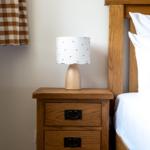 Schlafzimmer mit Holzbett, Nachttisch und Lampe mit weißem Schirm.