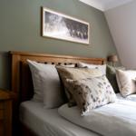 Schlafzimmer mit Holzbett, Kissen und Nachttisch. Wandbild über dem Bett.