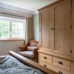 Schlafzimmer mit Holzbett, Kleiderschrank und Sessel vor Fenster mit Blick auf Bäume.