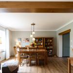 Esszimmer mit Holztisch, Stühlen und Bücherregalen. Holzdeckenbalken und helle Wände.
